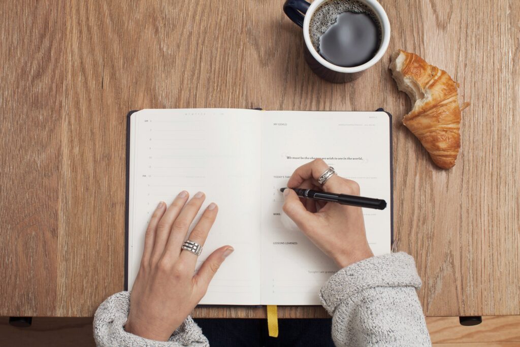 A person writing in a journal with a pen, seated in a cozy, naturally lit space — symbolizing self-reflection, mindful living, and emotional clarity through daily writing.