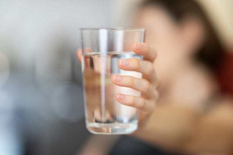 A hand offering a clear glass of water to another person, symbolizing kindness, hydration, and mindful connection through a simple, nourishing act.