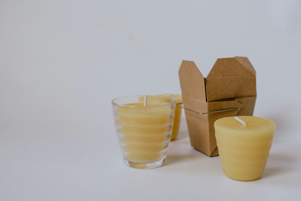 Hand-poured beeswax candle in a repurposed glass jar, resting on a wooden surface with dried flowers beside it.