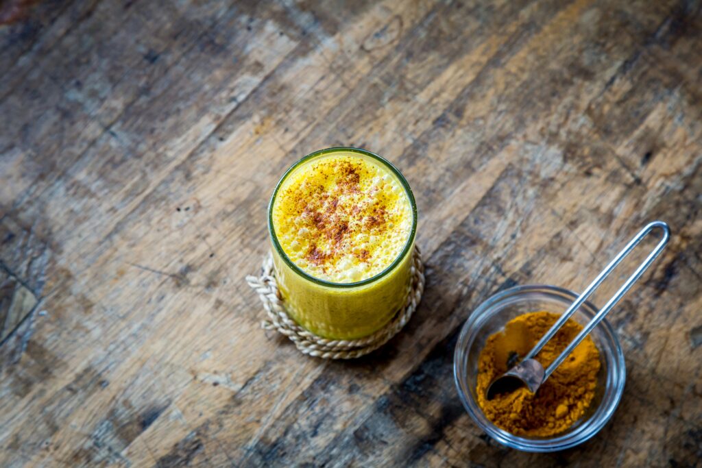 Golden milk in a ceramic cup with cinnamon garnish, served on a wooden tray.