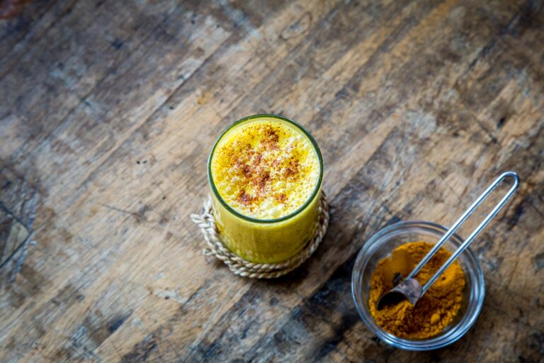 Golden milk in a ceramic cup with cinnamon garnish, served on a wooden tray.