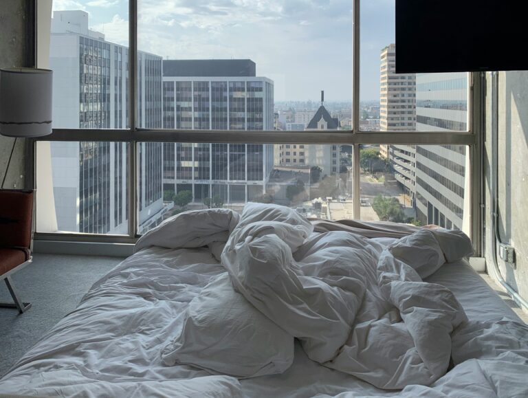 A sunlit bedroom featuring a cozy bed with natural linens, bathed in morning light, promoting restful sleep and an early start to the day in harmony with nature